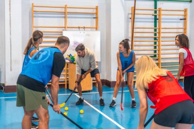 Spor salonunda antrenörleriyle oyun stratejisi uygulayan florbol takımı performanslarını artırmak için takım çalışması ve beceri geliştirmeye odaklanıyor.