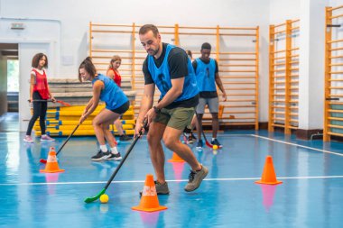 Bir grup sporcu spor salonunun içinde yoğun bir antrenman sırasında sopalarla koşup ustalıkla topa vuruyorlar.