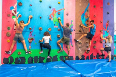 Spor salonunda kaya duvarına tırmanan beş sporcu, eğlenceli ve aktif bir deneyim yaşarken tırmanma becerilerini geliştirmek için birlikte antrenman ve egzersiz yapıyorlar.