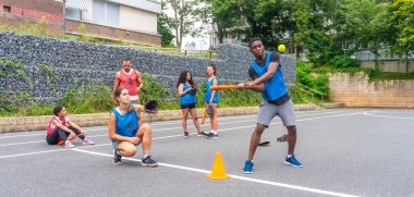 Kentsel bir sahada antrenman yapan çok ırklı beyzbol oyuncuları, topa vuran bir vurucu ve takım çalışması ve atletizmi ön plana çıkarmaya hazır bir yakalayıcı ile