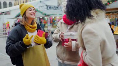 Arkadaşlar hediye alışverişi yapıyor, kış mevsiminde şenlikli şehir tatil pazarında üstlerinde kışlık giysiler ile birbirlerine sarılıyorlar.