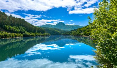 Huzurlu ibiur rezervuarı bereketli yeşil tepelerin ve tüylü beyaz bulutlarla kaplı parlak mavi gökyüzünün manzarasını yansıtıyor, Tolosa, Bask ülkesinde nefes kesici bir manzara yaratıyor.