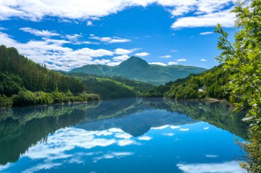 Ibiur rezervuarının sakin suları canlı mavi gökyüzünü ve çevresini saran yemyeşil dağları mükemmel bir şekilde yansıtıyor. Tolosa, Bask ülkesinde sakin ve görkemli bir manzara yaratıyor.