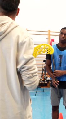 Koçun yanında duran dikkatli florbol oyuncuları, sopayı kavrayıp dikkatle odaklanırken jimnastik salonunda stratejik talimatlar alıyorlar.