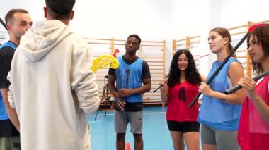 Profesyonel zemin topu takımı dikkatle toplanıyor, modern spor salonundaki antrenman sırasında deneyimli koçun stratejik rehberliğini dinliyorlar.