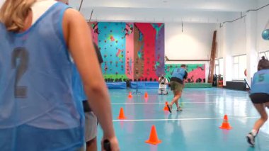 Numaralı forma giyen sporcular hareketli bir hokey maçına katılıyorlar, turuncu koniler etrafında iç mekandaki bir spor salonunda canlı bir mavi kortta manevra yapıyorlar.