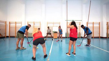 Amatör atletler, yer hokeyi antrenmanında. Yoğun pas ve şut atma, takım çalışması ve aydınlık spor salonunda atletizm yetenekleri.