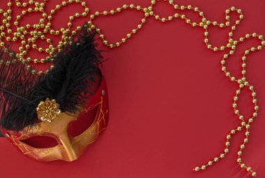Maskeli balo maskesi ve altın boncuklu Noel kırmızı arka planı. Düz yatış stili. Yeni yıl maskeli davetiye kartı.