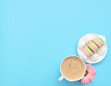 Bir fincan kapuçino ve pembe çiçekli mavi arka planda beyaz tabakta beyaz merengeli lezzetli badem kurabiyeleri. Mutlu günler, kahvaltı kavramları. Tebrik kartı. Kopya alanı ile düz uzanma biçimi.