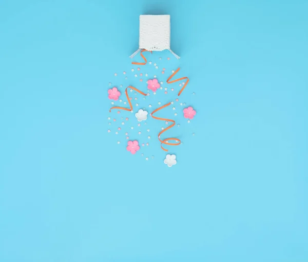 White box with party confetti, streamers and flowers explosion on blue background. Mother day, Valentine day, Wedding, Birthday party concept. Greeting or invitation card. Flat lay with copy space.