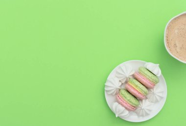 Bir fincan kapuçino ve yeşil arka planda beyaz tabakta beyaz merengue 'li lezzetli badem kurabiyeleri. Mutlu günler, kahvaltı, günaydın kavramları. Tebrik kartı. Kopya alanı ile düz uzanma biçimi.