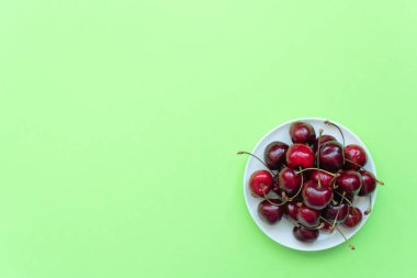 Yeşil arka planda beyaz tabakta taze kirazlar. Sağlıklı beslenme, minimalizm kavramları. Metnin için kopyalama alanı olan düz konum biçimi.
