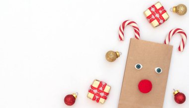 Hüner çantasından yapılmış Noel geyiği ve hediye kutularıyla birlikte iki Noel bastonu, beyaz arka planda kırmızı ve altın toplar. Yeni yıl tebrik kartı. Noel ve Yeni Yıl konsepti. Kopya alanı ile düz uzanma biçimi.