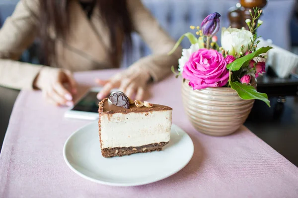 Creamy cheesecake with chocolate cookies and cream biscuits. Oreo cake and a beautiful vase with flowers on the table. A beautiful bouquet of flowers. Hands of the girl with the phone.