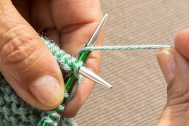 Dairesel iğneler kullanarak örgü ören ellerin yakın çekimi.