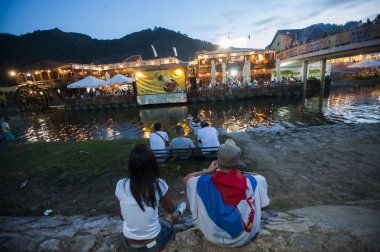 Guca, Sırbistan - 8 Ağustos 2015: Genç çift, Sırp bayrağıyla kaplanmış, Sırbistan'daki Guca Trompet Festivali sırasında bir nehrin kıyısında oturun