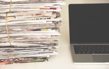 Gazeteler ve laptop. Bilgisayarın yanında haberleri olan bir yığın günlük gazete. Modern cihazlar ve eski günlükler, gazetecilere odaklan.