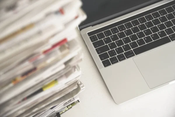 Gazeteler ve laptop. Bilgisayarın yanında haberleri olan bir yığın günlük gazete. Modern cihazlar ve eski günlükler, dizüstü bilgisayara odaklan.