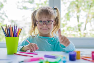 Küçük kız bir pencere bir odası için boyalar ve boya kalemi çizim. Şirin çocuk ödev yapmak. Yaratıcı çocuk. Kız gösteren Ok işareti.