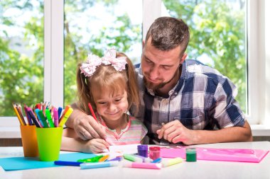 Kızının okul öncesi çağda yardımcı olmak için renk kağıt mutfak üzerinde genç olumlu sakallı adam. Mutlu bir aile.
