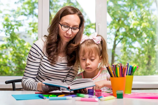 Mutlu bir aile. Anne ve kızı birlikte boya. Anne ve kızı bir kitap ev ödevi. Kadın kız çocuk yardımcı olur..