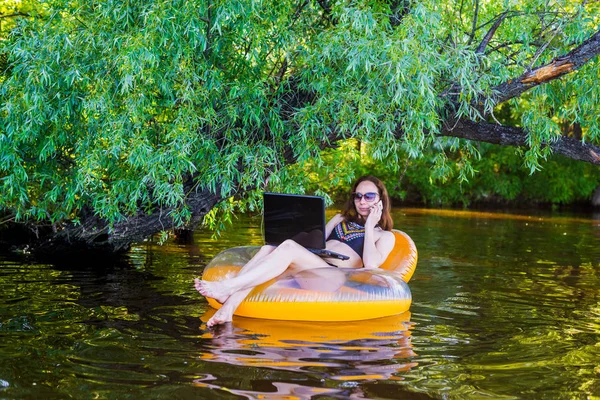 Manager working on vacation, free space. Woman workaholic working on a laptop sitting in an inflatable ring.