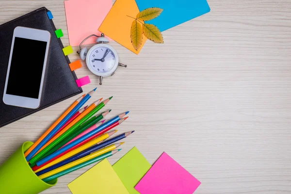 Okul kırtasiye masa üstü görünümünde kümesi. Renk kağıt, kalem, ahşap bir masa, boş alan smartphone.