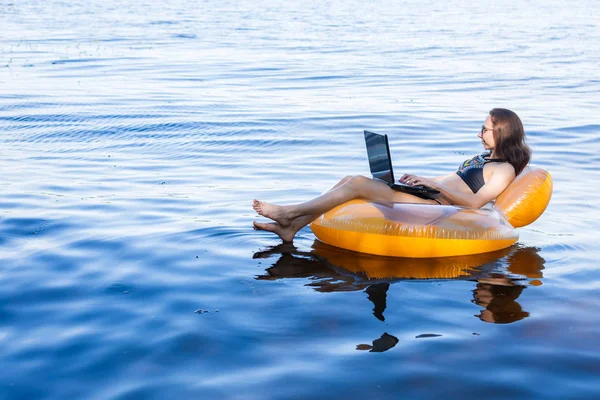 Denizde, tatilde çalışma kavramının şişme bir ringde bir dizüstü bilgisayar üzerinde çalışan iş kadın. Kadın işkolik.