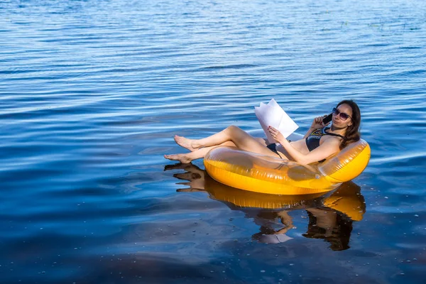 Tatil sırasında çalışma işkolik bir kadındır. Denizde şişme ringde siting ve Evet, iş kadını boş alan.