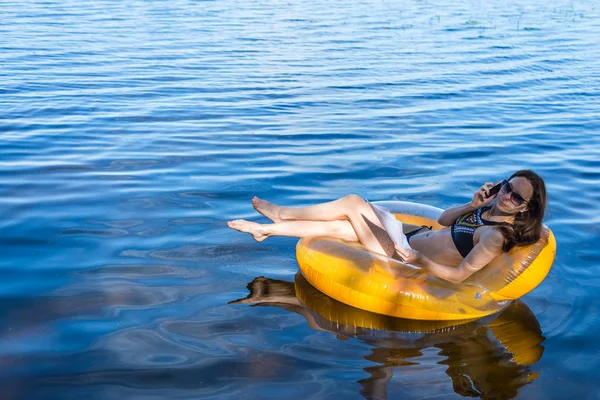 Woman is workaholic working during the vacation. Business woman siting in inflatable ring at sea and talking on the phone, free space.