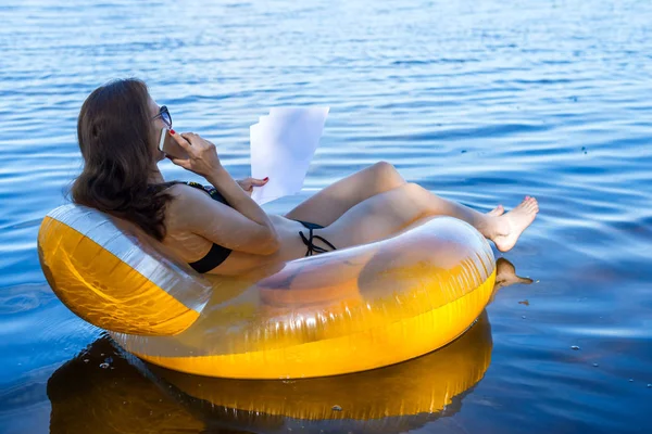 Business woman working on vacation, remote work. Woman talking on mobile phone while sitting in an inflatable ring