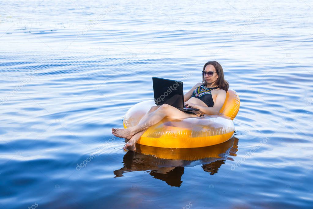 Business woman working on a laptop in an inflatable ring on the sea, the concept of working on vacation. Woman workaholic.