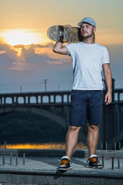 Güzel bir gün batımı arka plan üzerinde kaykay ile ayakta genç şık kaykaycı. Aktif yaşam tarzı.