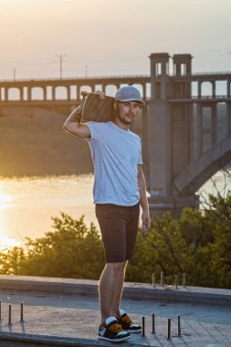 Güzel bir gün batımı arka plan üzerinde kaykay ile ayakta genç şık kaykaycı. Aktif yaşam tarzı.