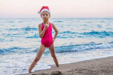 Sevimli kız sahilde bir şapka Santa Claus, Noel ve yeni yıl kutluyor boş alan. Noel arka plan, tropikal ülkelerde kış tatili.