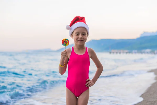 Noel arka plan: sahilde, Noel ve yeni yıl kutlama Noel Baba şapkası şirin çocuk boş alan. Kış tatil tropikal ülkelerde. Noel şapka ve bir lolipop kız.
