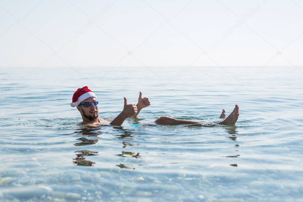 Man in a Santa Claus hat and glasses for swimming, christmas background. Relax in tropical countries in the winter, New Year's weekend.
