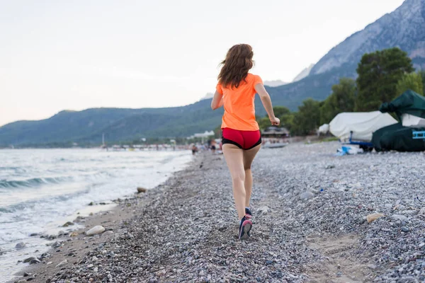 Estilo de vida activo: una mujer delgada corre por la playa . — Foto de Stock
