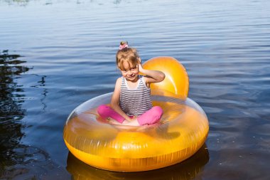 Küçük kız şişme bir sandalyede oturan bir cep telefonuyla konuşuyor.