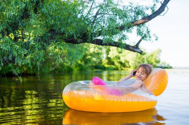Küçük kız bir telefon şişme bir sandalyede oturup, konuşurken.