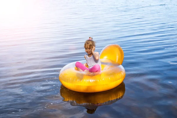 La niña está descansando en una silla inflable en el agua. El niño está hablando en el teléfono inteligente . — Foto de Stock