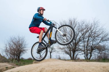 Mavi bir kazak ve kırmızı şortlu genç bisikletçi kir üzerinde sürme.