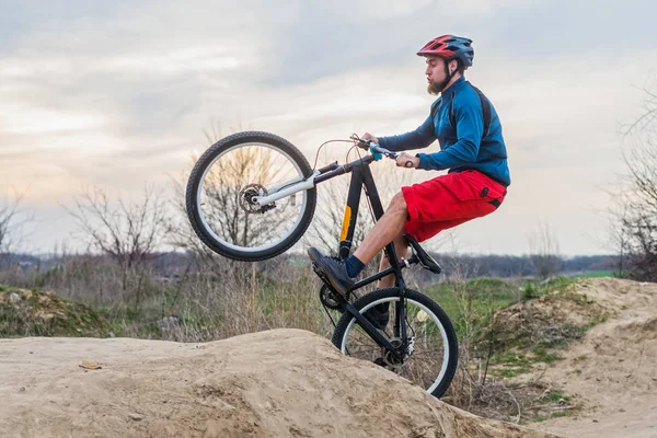 Man på en mountainbike i röda shorts och blå tröja utför ett smuts hopp. Aktiv livsstil. — Stockfoto