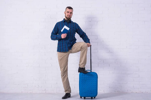 Мужчина с голубым чемоданом и паспортом возле стены из белого кирпича . — стоковое фото