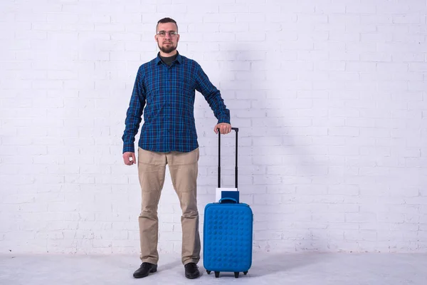 Ein Mann mit blauem Koffer und Pass in der Nähe einer weißen Backsteinmauer. — Stockfoto