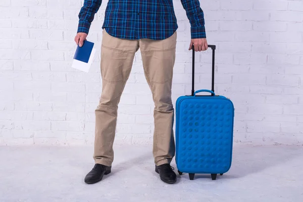 Ein Mann mit blauem Koffer steht in der Nähe einer weißen Backsteinwand. Urlaub, freier Raum. — Stockfoto