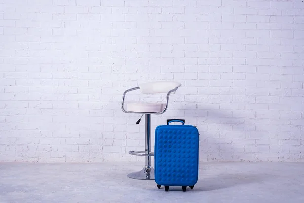 Blue suitcase and high chair near the white brick wall. Space for text — Stock Photo, Image