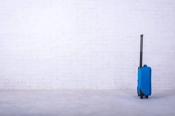 Niebieska walizka w pobliżu białej ściany z cegły. — Zdjęcie stockowe
