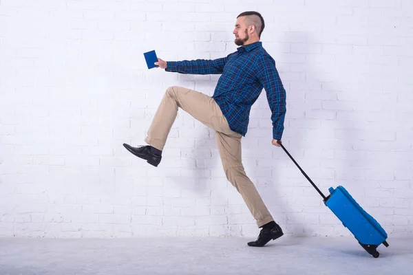 A man with a blue suitcase and a passport near a white brick wall. — Stock Photo, Image