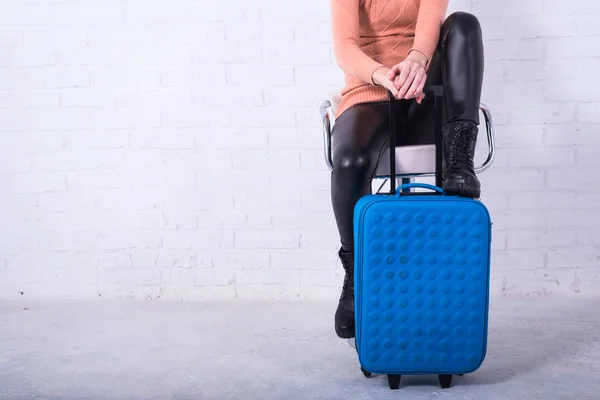 A woman with a blue suitcase is sitting on a chair, free space. — Stock Photo, Image